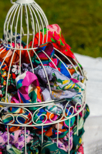 Barevné scrunchies Caloo vystavené v bílé kovové kleci na slunci, mix vzorovaných látek z viskózy a saténu, focené venku na trávě.