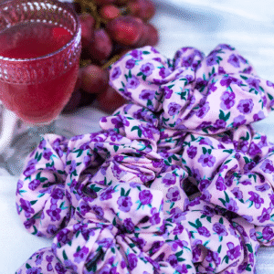 Gumičky Purple Blossom z viskózy s květinovým potiskem, naaranžované na látce vedle sklenice vína a hroznů