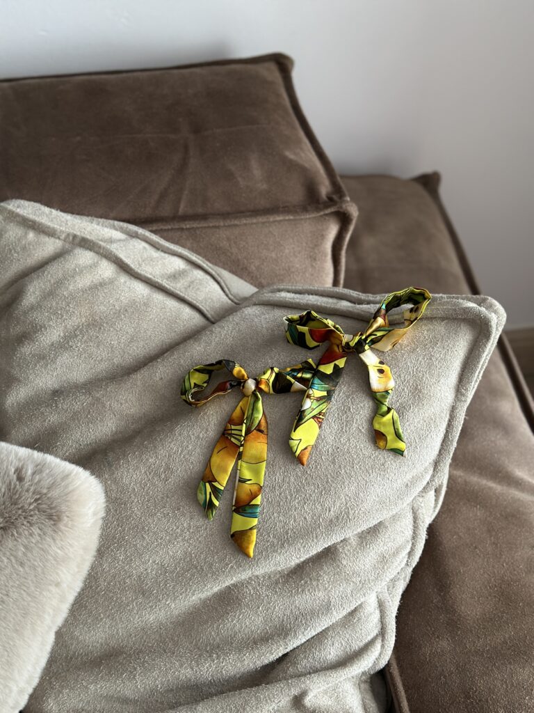 Dvě hedvábné mašličky Sweet Pear s ovocným potiskem, volně položené na sedačce