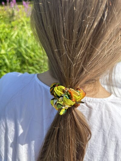 Scrunchie z kolekce Sweet Pear zachycená z profilu ve vlasech, s výrazným vzorem a hedvábným leskem.