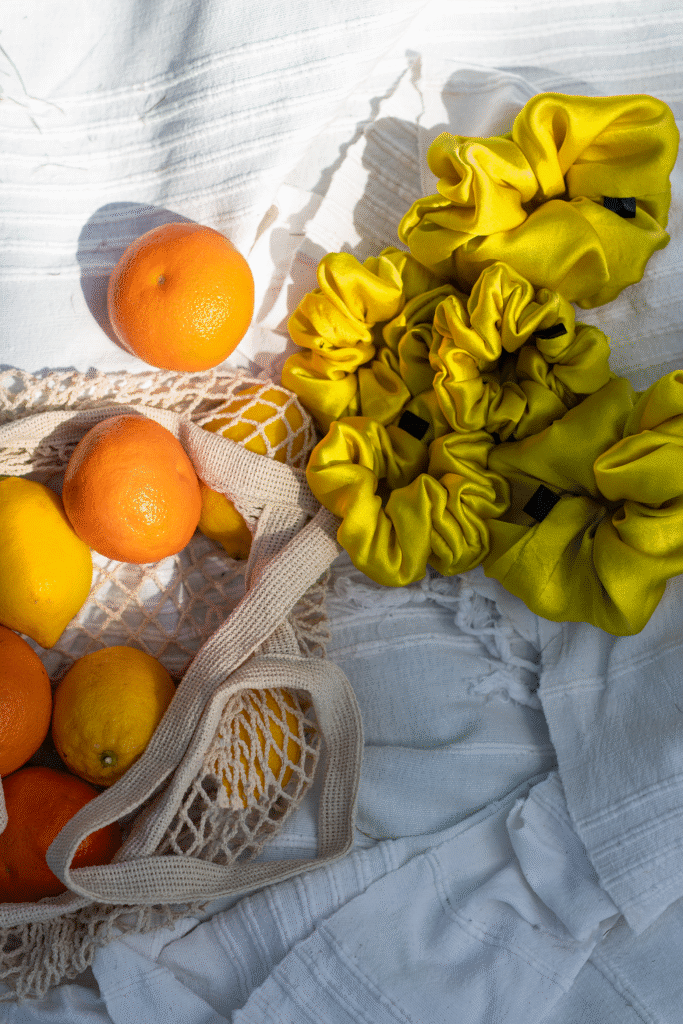 Kolekce žlutých hedvábných gumiček Sunny Silk ve velikostech S, M a L položená na bílé látce s ovocem – letní stylingový flatlay